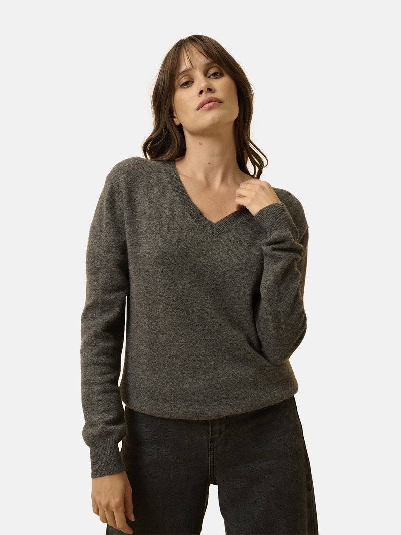 Maglione grigio in misto lana con scollo a V, maniche lunghe, polsini a coste e vestibilità rilassata, indossato sopra jeans scuri. Tessuto morbido, design minimal.