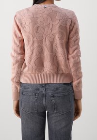 Pull tricoté rose clair texturé avec motifs floraux, poignets et ourlet côtelés. Le tissu est doux avec une coupe ajustée. L'arrière présente un petit détail métallique.