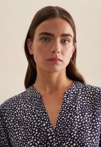 Blusa blu navy con scollatura a V e motivo astratto bianco. Il tessuto ha una texture liscia e una vestibilità comoda.