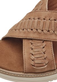 Sandalo in suede tan con design superiore intrecciato, punta aperta e cinturino posteriore. Presenta una suola in gomma beige e dettagli di cucitura decorativa.