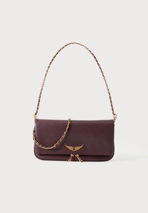 Σκούρο καφέ δερμάτινο clutch τσάντα με χρυσή αλυσίδα και χρυσό έμβλημα με φτερά στο μπροστινό μέρος, σε απλό ανοιχτό φόντο.
