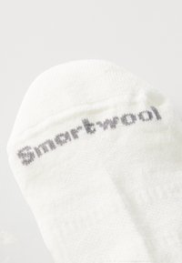 Valkoinen villasukka, jossa on tekstuurineulonta. "Smartwool" on brodeerattu harmaalla varren yläosaan. Yksinkertainen muotoilu ilman lisäkuvioita.