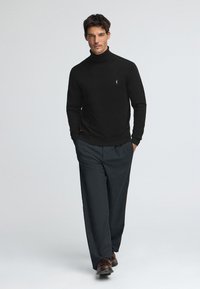 Svart polo tröja kombinerad med mörkgrå byxor. Outfiten har en figursydd design och en subtil varumärkeslogotyp på bröstet. Bruna skor kompletterar looken.