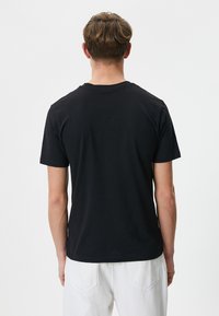 Sort bomulds t-shirt med korte ærmer, rund hals og en ensfarvet ryg, parret med hvide bukser, hvilket viser et afslappet design.