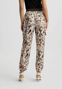 Leopardmønstret bukser i lys beige og brun. Elastisk talje, sidelommer og tapered manchetter. Glat, let stof.