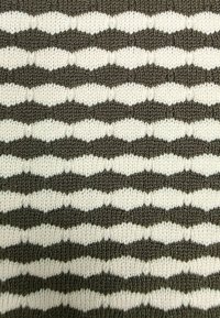 Dzianina z naprzemiennymi wzorami zygzaków w kolorze ciemnobrązowym i białym. Tekstura jest miękka, o wyglądzie grubej przędzy.