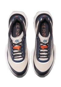 Sportiga sneakers med en beige och marinblå design, ovandel i mesh, texturerade mönster, svarta snören och en orange accent på tungan.