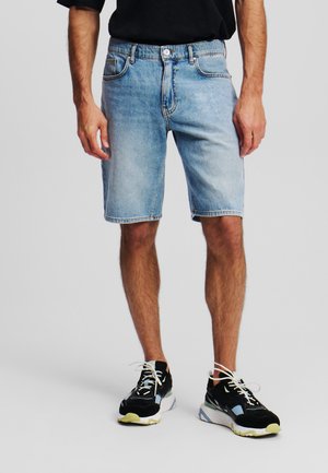 Shorts di denim blu chiaro con un taglio dritto, design a cinque tasche e cuciture visibili, abbinati a sneakers sportive nere.
