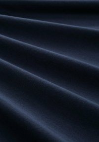 Ciemnoniebieska tkanina o gładkiej fakturze, prezentująca liczne fałdy i fale, ukazujące miękki, matowy wygląd.
