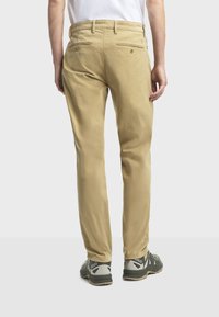 Khaki-Hosen mit geradem Schnitt aus Baumwolle, zwei Gesäßtaschen mit Knopfverschluss und kombiniert mit grauen Outdoor-Schuhen.