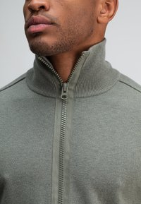 Groene, ritsjack met hoge kraag, voorzien van een gestructureerde breisel, geribde accenten en een gladde rits aan de voorkant.