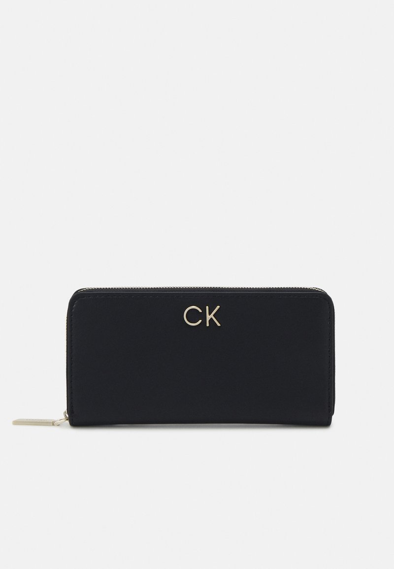 Portafoglio nero con zip, logo "CK" dorato, texture liscia, forma rettangolare e un piccolo dettaglio della zip.