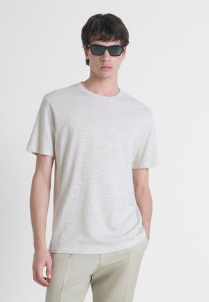 T-shirt rayé gris clair en tissu doux, à manches courtes et col rond, associé à des lunettes de soleil noires et un pantalon beige clair.