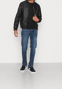 Chaqueta bomber de cuero negra con puños y cuello acanalados, combinada con jeans de mezclilla azules y zapatillas deportivas negras con acentos blancos.