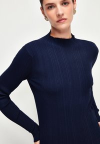 Mörkblå ribbad stickad tröja med långa ärmar och hög krage. Har en åtsittande passform och texturerad tyg. Utrustad med en kragefri design.