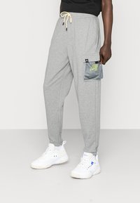 Graue Jogger-Hosen mit schmal zulaufendem Bein, elastischem Bund und verstellbarem Kordelzug. Mit einer Mesh-Cargotasche mit Logodetail.
