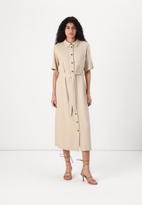 Abito button-up in misto lino beige con maniche corte, cintura con nastro e tasca frontale, abbinato a sandali con tacco alto beige con lacci.
