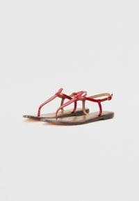 Red leather sandals with two thin straps crossing over the foot and a back strap. The insole features a textured pattern. Flat sole.