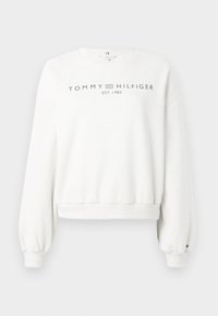 Hvit hettegenser med lange, litt puffede ermer. Har rund halslinning og trykt "TOMMY HILFIGER EST. 1985" logo i mørk grå.
