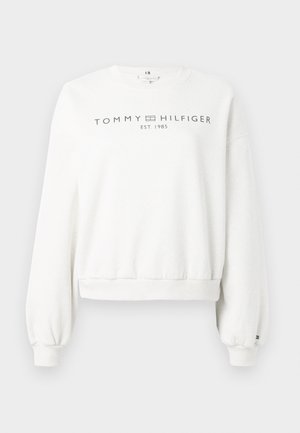 Balta džemperis su ilgomis, šiek tiek pūstomis rankovėmis. Turi apvalią iškirptę ir tamsiai pilką spaudą "TOMMY HILFIGER EST. 1985".