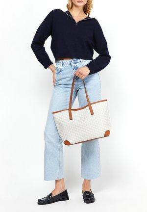 Bolso tote beige con un patrón texturizado, acentos de cuero marrón, combinado con un suéter cropped azul marino y jeans de cintura alta azul claro.