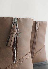 Botas de cuero marrón con cremalleras laterales, una cremallera tiene un borlas y un charm metálico en forma de estrella adjunto.