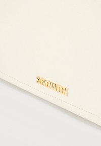 Υφασμα σε απόχρωση κρέμα με ένα μικρό χρυσό μεταλλικό λογότυπο «Steve Madden» τοποθετημένο κοντά στο κάτω άκρο.