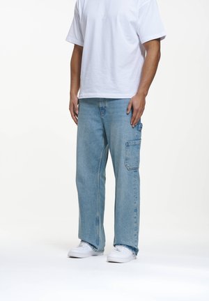 Lysblå denim cargo bukser med en afslappet pasform, der har en sidelomme, båret med en hvid t-shirt og hvide sneakers.