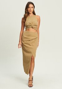Tvådelad outfit i ljusbrunt tyg. Crop-toppen har en vriden design framtill, och kjolen har en slits på ena sidan.