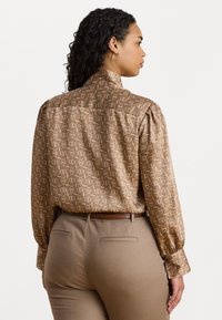 Brunmønstret bluse med lange ærmer og høj krave. Har et geometrisk design i lysere nuancer, glat stof, og en afslappet pasform.