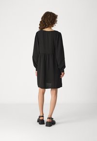 Vestido preto com mangas bufantes longas, cintura ajustada e comprimento até os joelhos. Textura suave, decote redondo e detalhes de costura subtil.