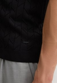 Czarny sweter z dzianiny z teksturowanym wzorem liści, z ribbowanym wykończeniem. Zawiera małą metkę z logo blisko dolnej krawędzi.