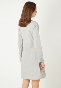 Vestido gris claro, hasta la rodilla, con mangas largas, que presenta puños plisados y detalles laterales. Textura suave y ajuste entallado.