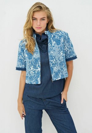 Kék farmerdzseki virágmintával, rövid ujjakkal és rojtos szegéllyel. Sötétkék felsővel és hozzáillő nadrággal párosítva.