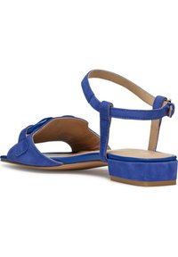 Sandale en Suède bleue avec un bout ouvert, une bride ajustable à la cheville et un petit talon carré. Présente un design courbé et une texture lisse.