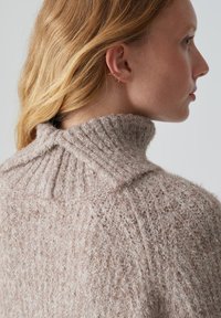 Helles rosa, strukturiertes Strickpullover mit hohem Kragen und geripptem Design. Weiches Material mit einer flauschigen Oberfläche und dezentem Detail.