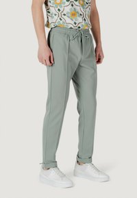 Pantaloni jogger verde chiaro con cintura elastica, chiusura con lacci e design affusolato. Indossati con sneakers bianche e top a fantasia.