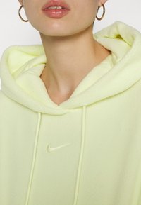 Sudadera de forro polar amarillo claro con una gran capucha, cordones y un pequeño logotipo de Nike bordado en el pecho. Textura suave.