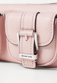 Ružová pebbled kožená peňaženka s obdĺžnikovým tvarom, vybavená metalickým strieborným prackou a štítkom "MICHAEL KORS" vpredu.