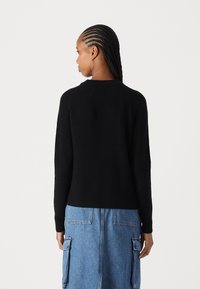 Schwarzer gerippter Pullover mit Crew-Ausschnitt, leicht taillierter Form und langen Ärmeln, kombiniert mit einem blauen Jeansrock mit Taschen.