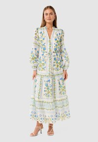 Long-sleeve floral dress featuring blue flowers and green leaves on a light background, with a tie waist and tiered hem. Open collar and buttons.