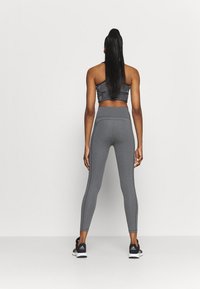 Leggings atléticos grises con una cinturilla alta, tela texturizada y costuras laterales. Combinados con un sujetador deportivo negro cortado y zapatillas negras.