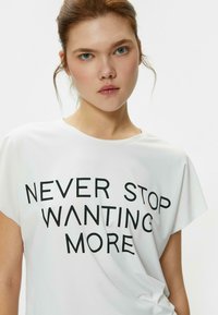 Camiseta blanca de manga corta con un corte relajado. Presenta un texto en negrita de color negro "NUNCA DEJES DE QUERER MÁS" centrado. Textura suave y lisa.