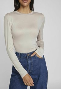 Långärmad beige topp i mjukt material, kombinerad med högmidjade mörk denimjeans med knapp- och fickdetaljer.