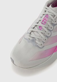 Világosszürke sportcipő rózsaszín részletekkel és csíkos mintával. Texturált anyagból, fűzőkkel és márkajelzéssel. Kerek orr és párnázott talp.