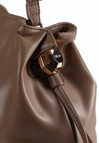 Sac en cuir brun avec un design froncé, mettant en valeur un détail en métal hexagonal brillant et une texture lisse. Les détails comprennent des coutures le long des bords.