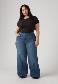 Fekete bordázott, rövid ujjú felső, magas derekú, bő szárú kék denim farmerrel párosítva. Az anyag sima, klasszikus kék mosással.