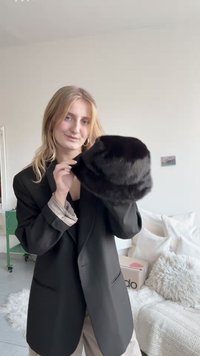 Musta karvamüts ümarate ja pehmete joontega. Tekstuur tundub pehme ja luksuslik, pehme läikega, mille hoiab käes inimene, kellel on seljas must bleiser.