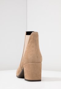 Tan mockasiner med blockklack, elastiska sidopaneler och en slät insida. Har rundad tå och subtila sömnadsdetaljer.