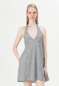 Rochie halter în carouri alb-negru, cu un decolteu adânc în V, design fără mâneci și buzunare pe lateral.